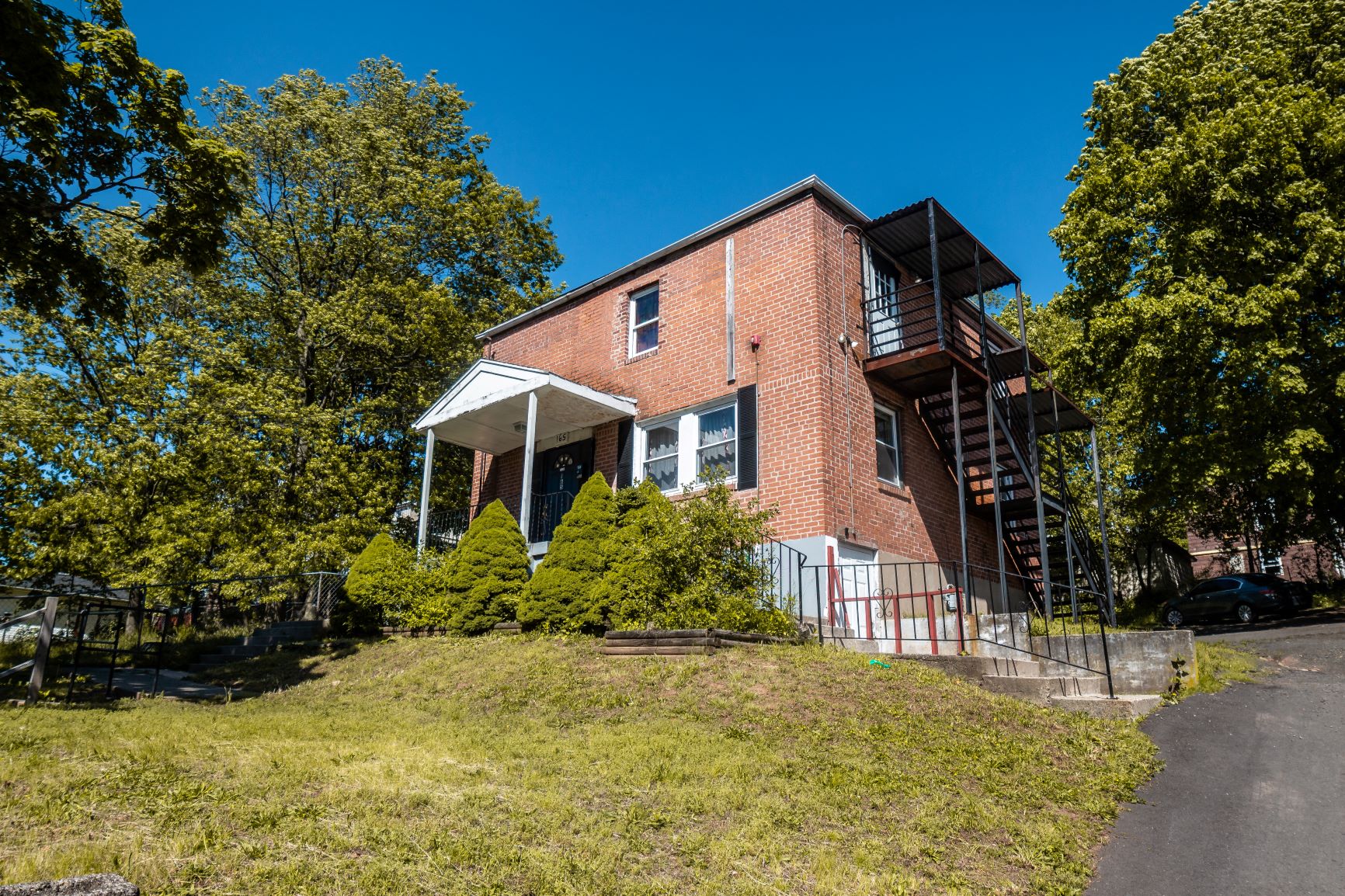 A red brick house with a white porch and a balcony on the second floor.