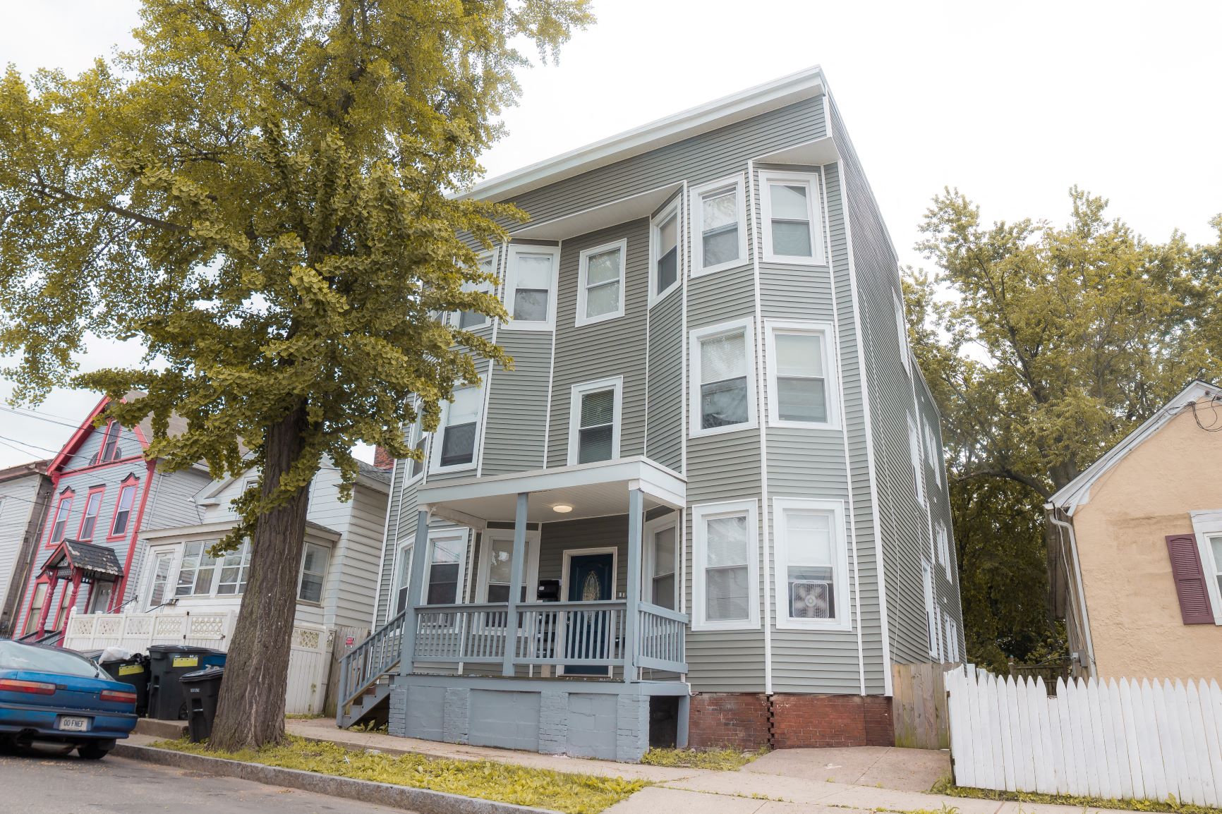 A grey two-story house with a balcony and a tree in front.