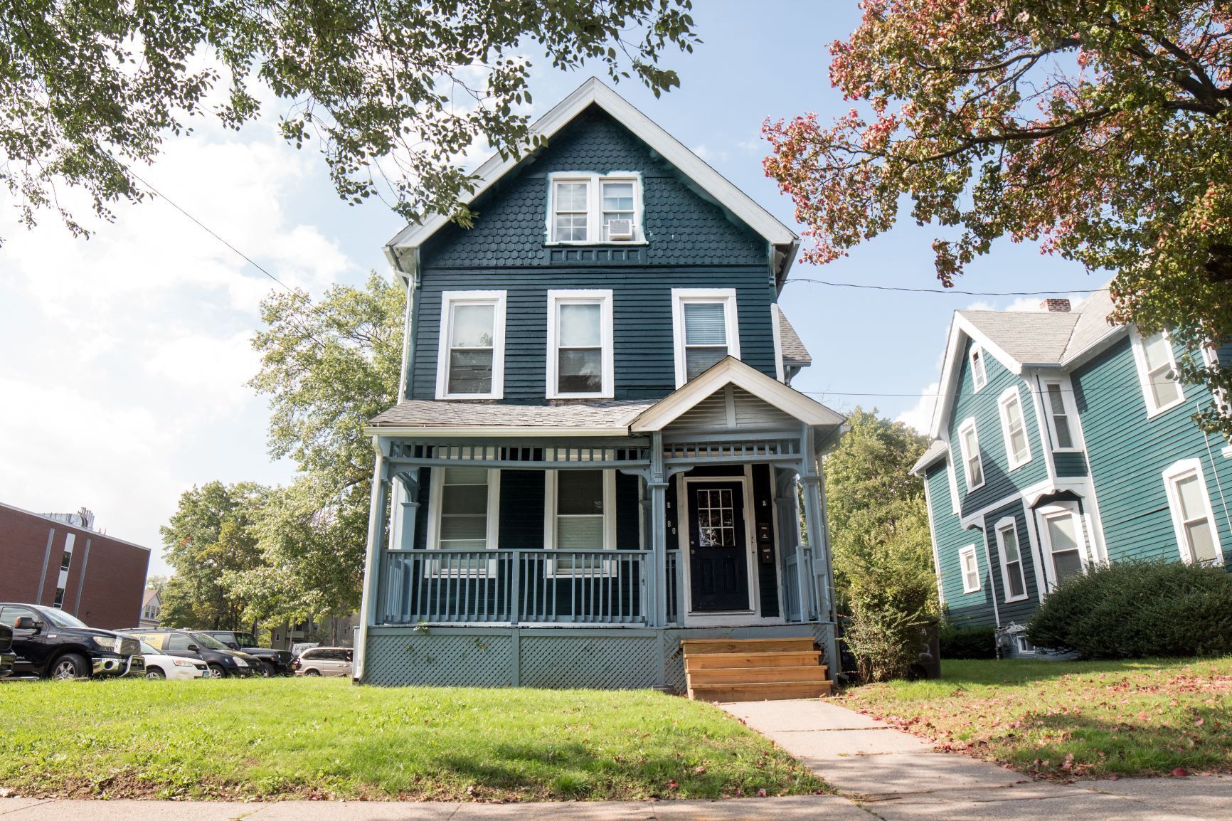 A blue house with a porch and a tree in front.