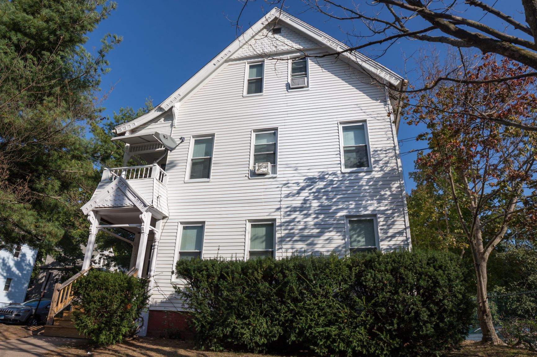 A white house with a porch and a tree in front.