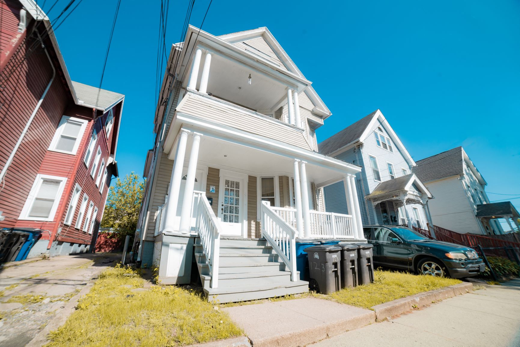 A white two-story house with a porch and a car parked in front.