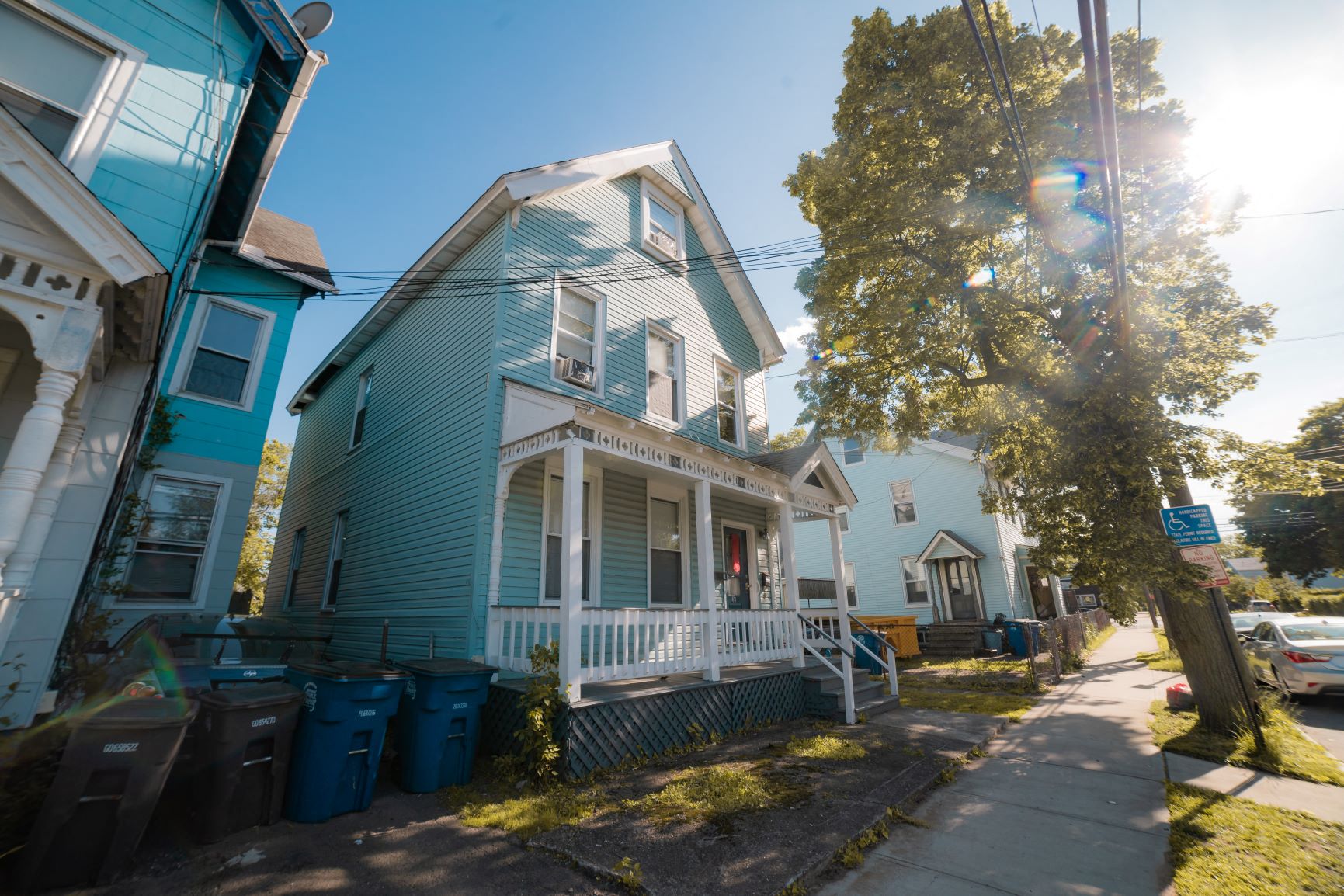 A blue house with a white porch and a tree in front.
