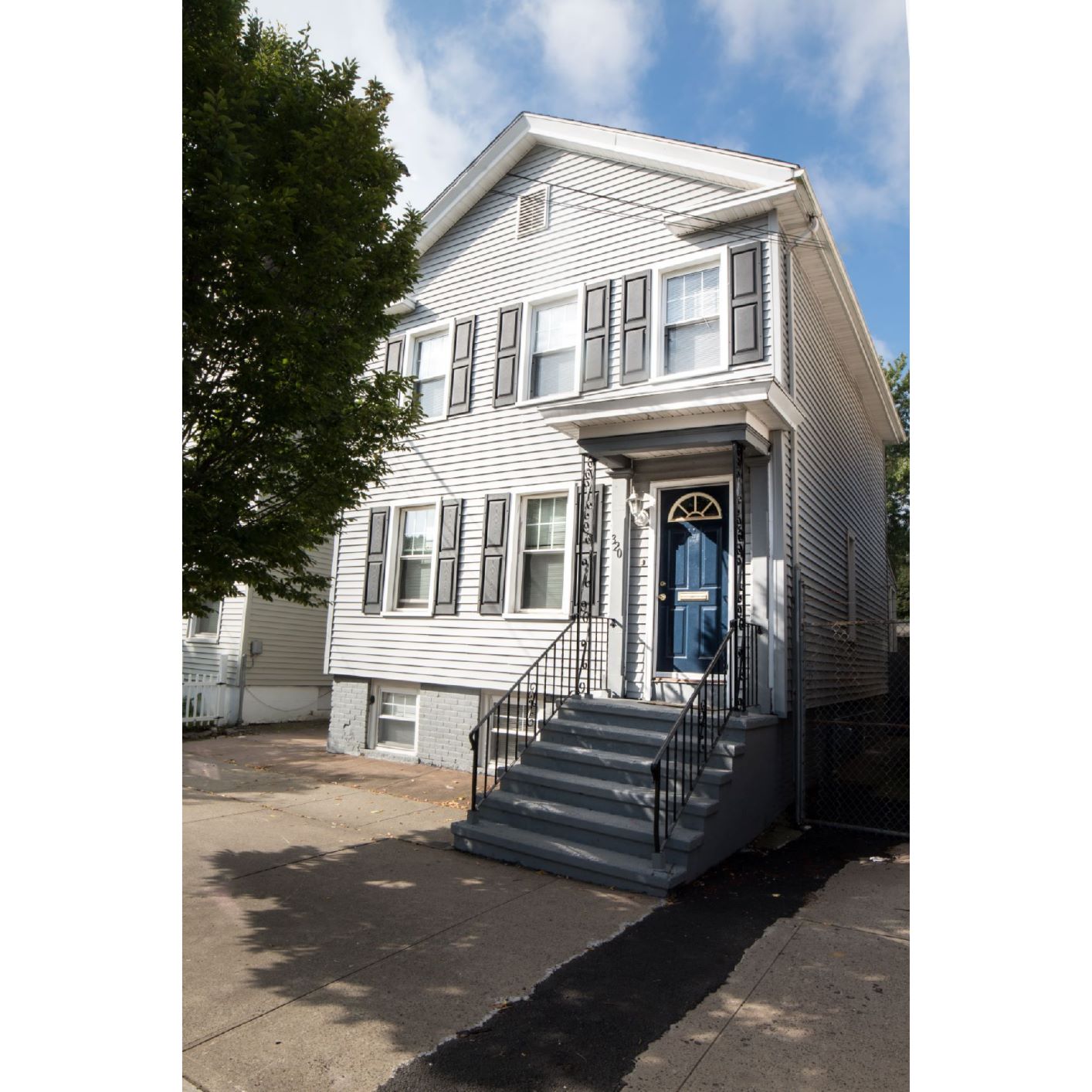 A two-story house with a blue door and a black metal railing on the stairs.