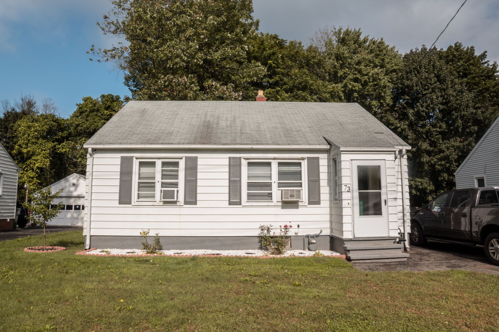 A small white house with a grey roof and a black truck parked in front.