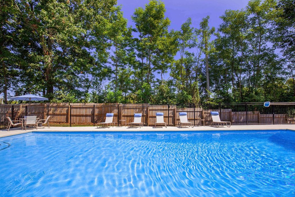 a swimming pool with chairs and trees in the background