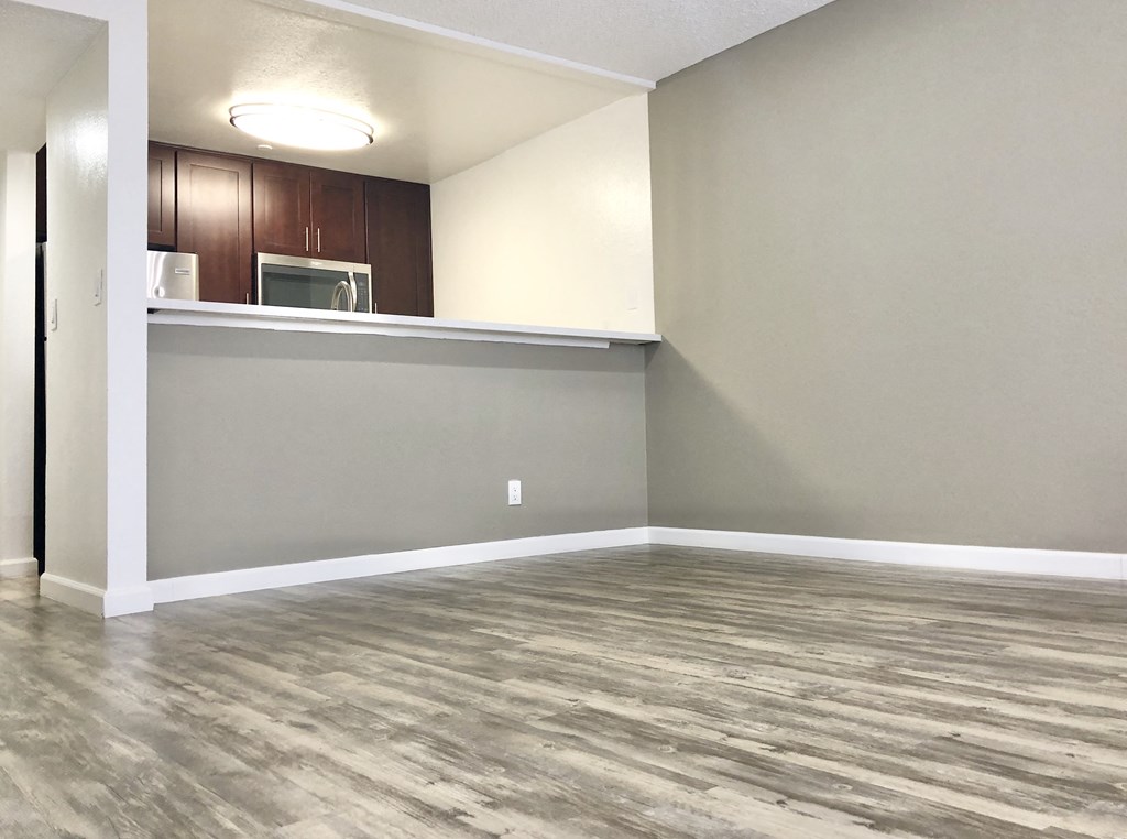 an empty living room with wood flooring and a kitchen