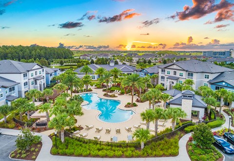 an aerial view of a large swimming pool with palm trees and buildings around it