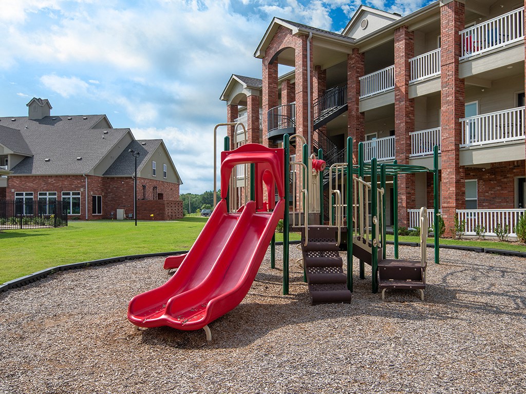 a playground with a red slide in front of an apartment building