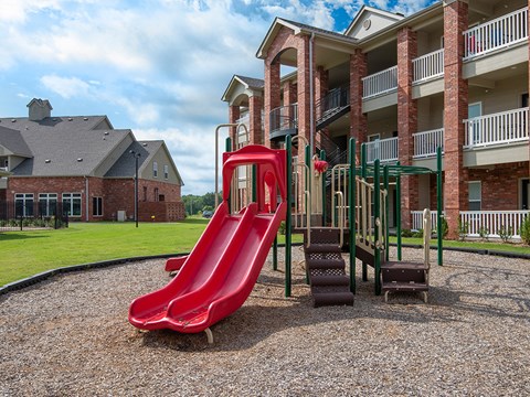 a playground with a red slide in front of an apartment building