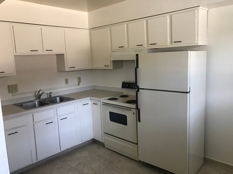 A white kitchen with a sink, stove, and refrigerator.