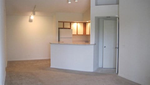 an empty living room with a kitchen and a door
