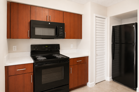 A black microwave is mounted above a black stove in a kitchen with wooden cabinets.
