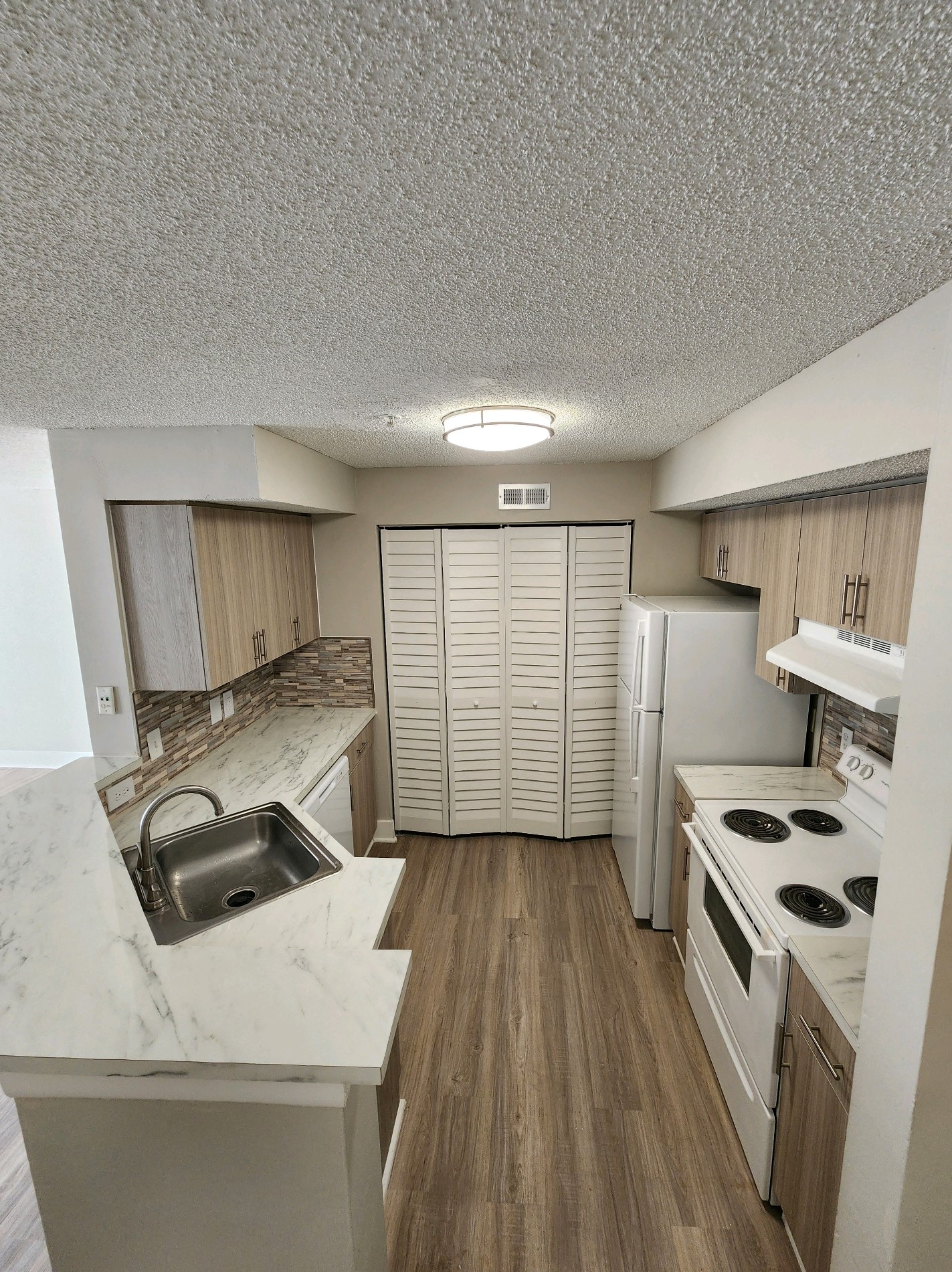 A kitchen with a white counter top and wooden floors.