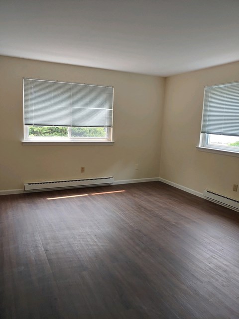 an empty room with wooden floors and two windows