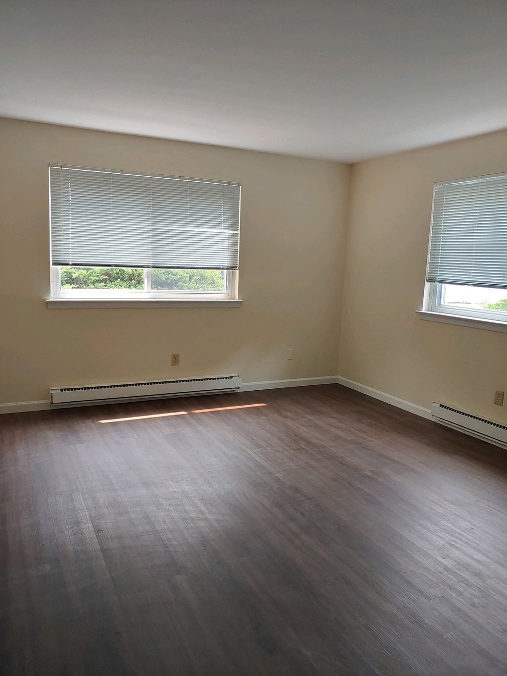 an empty room with wooden floors and two windows