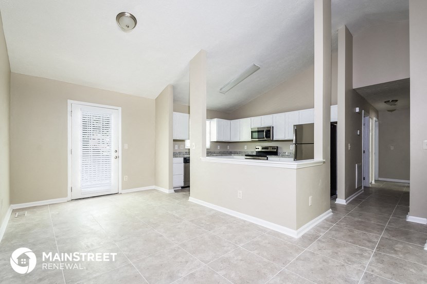 an empty living room with a kitchen and a door to a hallway