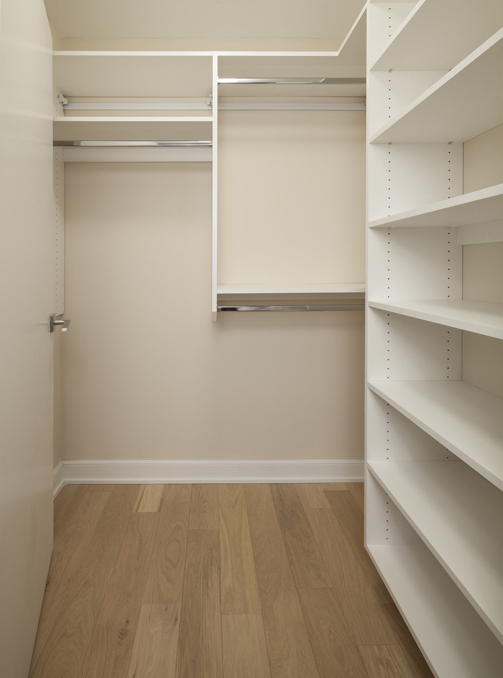 a walk in closet with white shelves and a wood floor