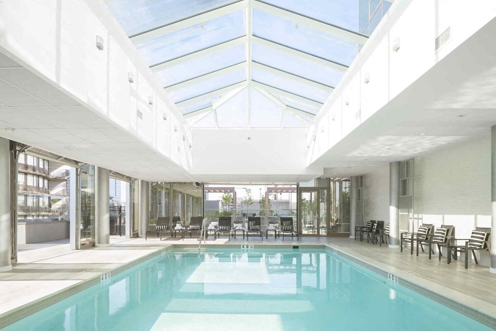 the pool is under a large glass roof in therium of a building with chairs