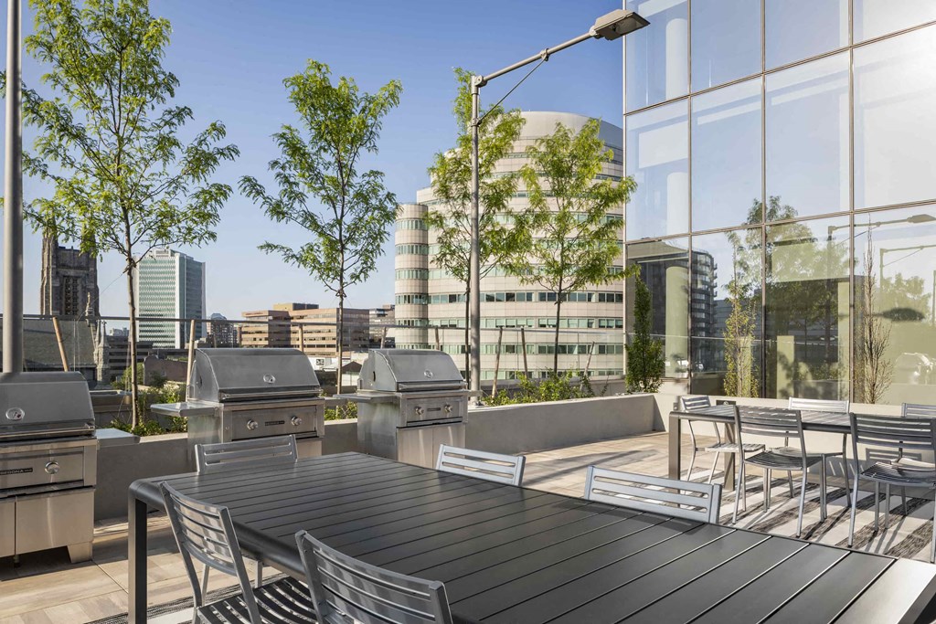 a patio with tables and chairs and barbecue grills on a rooftop