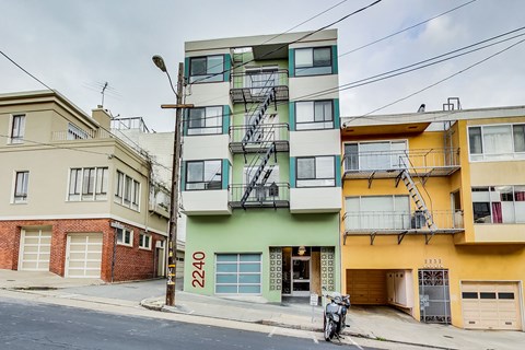 A street view of a residential area with buildings and a motorcycle parked on the sidewalk.