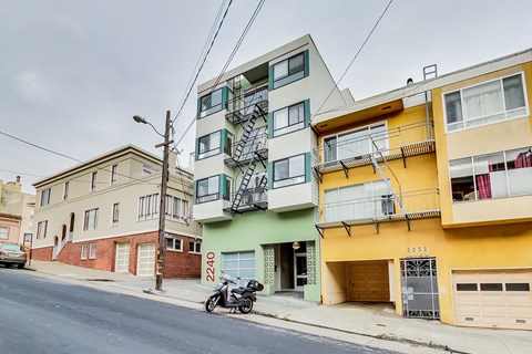 A motorcycle is parked on the sidewalk in front of a yellow building.