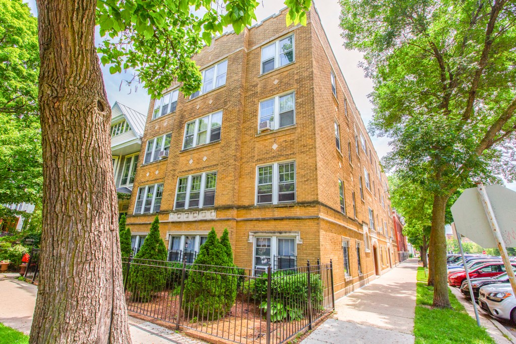exterior view of a brick apartment building with trees and a fence