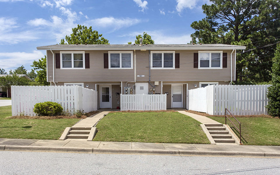 the front of a house with a lawn and a white fence