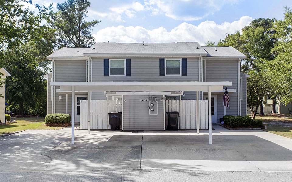 a gray house with a parking lot and a white fence