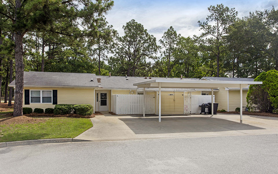 the front of a yellow house with a driveway and a covered porch