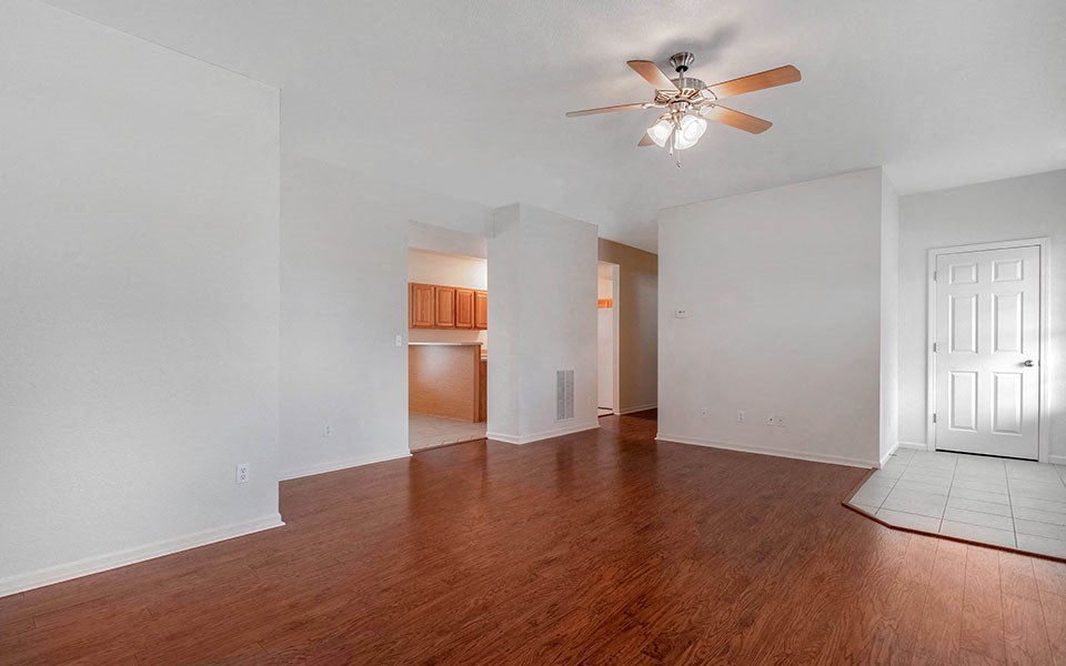 an empty living room with wood flooring and a ceiling fan