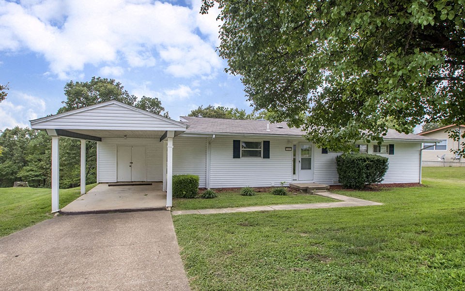 a small white house with a driveway and a tree