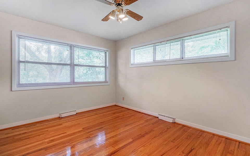 an empty room with a ceiling fan and two windows