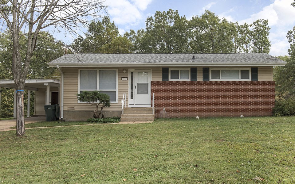 the front of a brick house with a lawn and trees