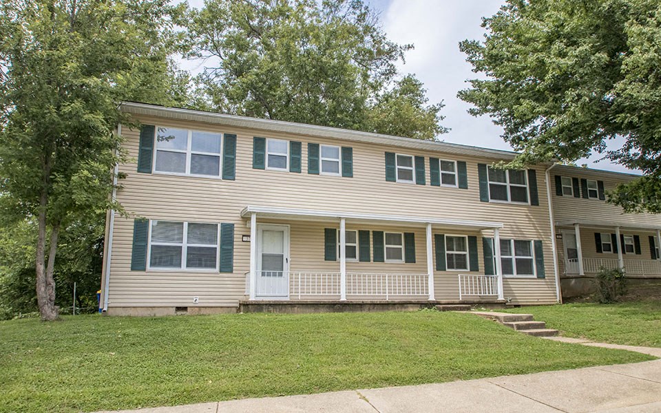 a tan house with green shutters and a lawn
