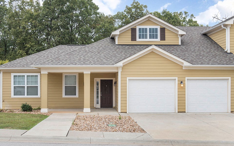 a tan house with two garage doors and a driveway