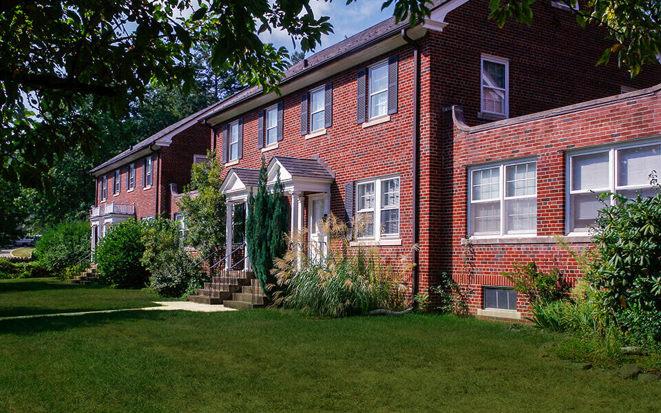 the front of a red brick house with green grass and trees