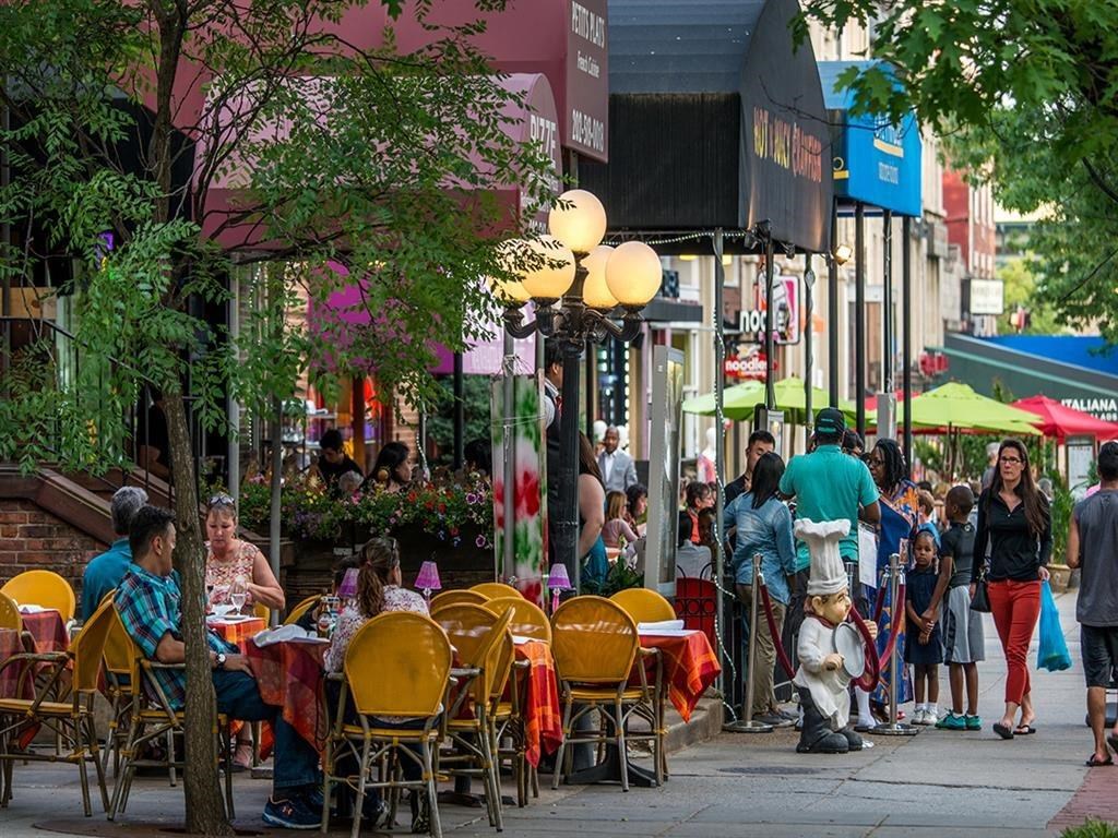 people walking and sitting at tables and chairs on a city street