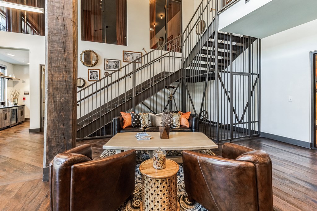 a living room with leather chairs and a table     and a staircase