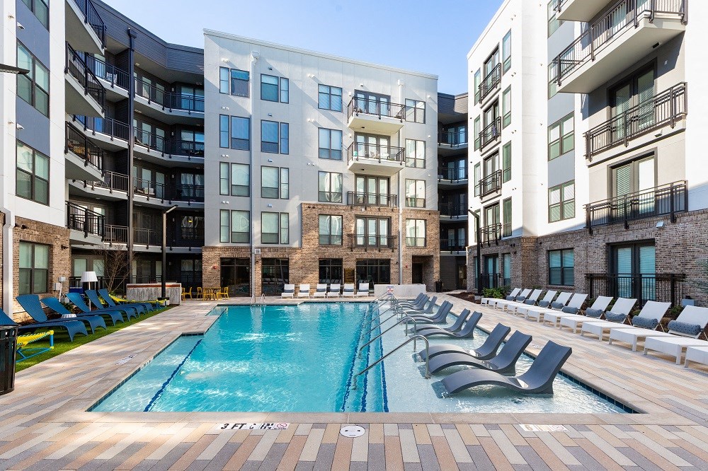 an outdoor pool with lounge chairs in front of an apartment building