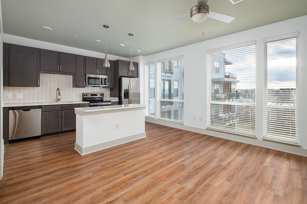 an empty living room with a kitchen and a large window