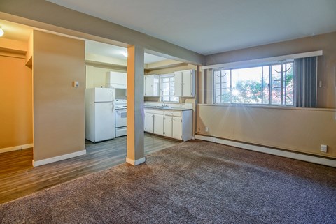 an empty living room with a kitchen and a window
