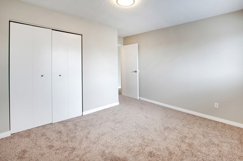 an empty bedroom with white closet doors and carpeting