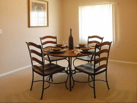 A dining table with four chairs and a bottle of wine on it.