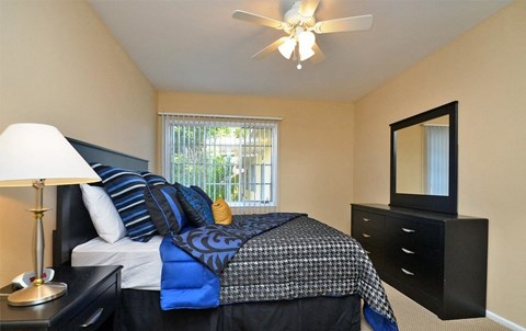 A bedroom with a bed, dresser, mirror, and a ceiling fan.
