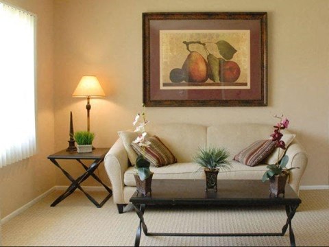A living room with a couch, coffee table, and a painting of fruit.