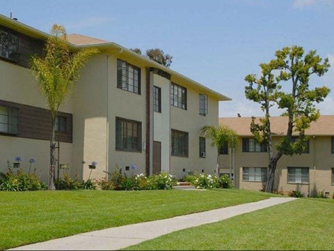 A row of beige apartment buildings with green lawns in front.