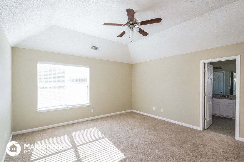 an empty living room with a ceiling fan and a door to a bathroom