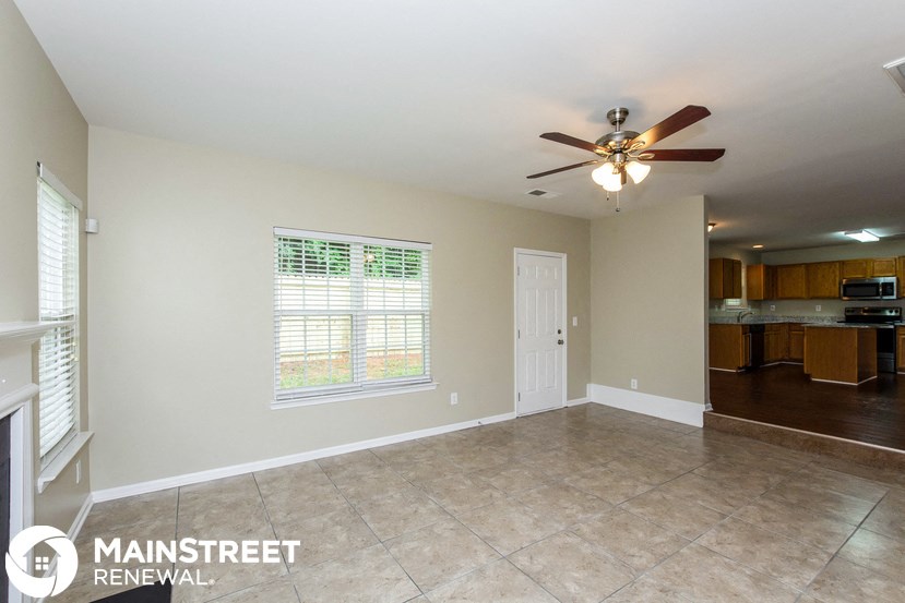 an empty living room with a ceiling fan and a kitchen
