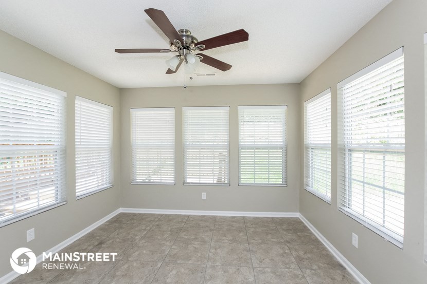 an empty living room with a ceiling fan and large windows