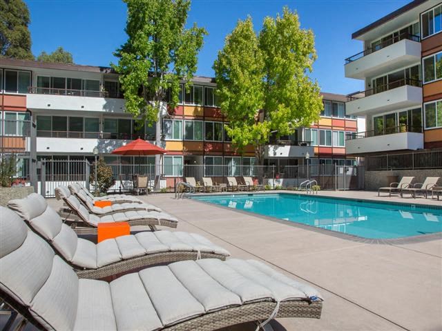 a pool and lounge chairs in front of an apartment building